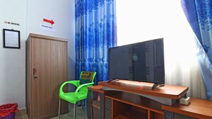 A room with a wooden cabinet, a green chair, a television on a wooden stand, and a blue curtain.