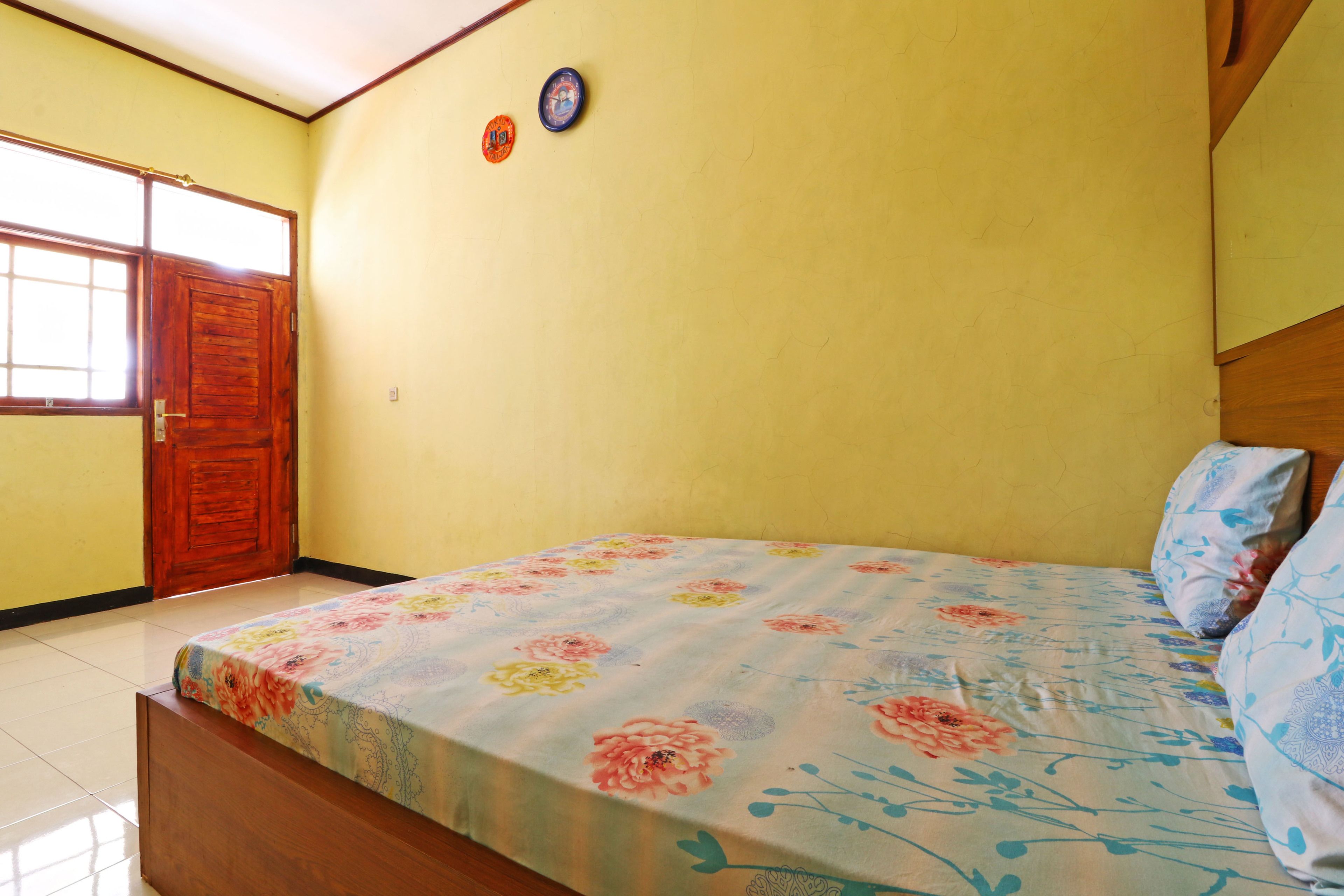 A bedroom with a floral bedspread, wooden headboard, and a door with a window.