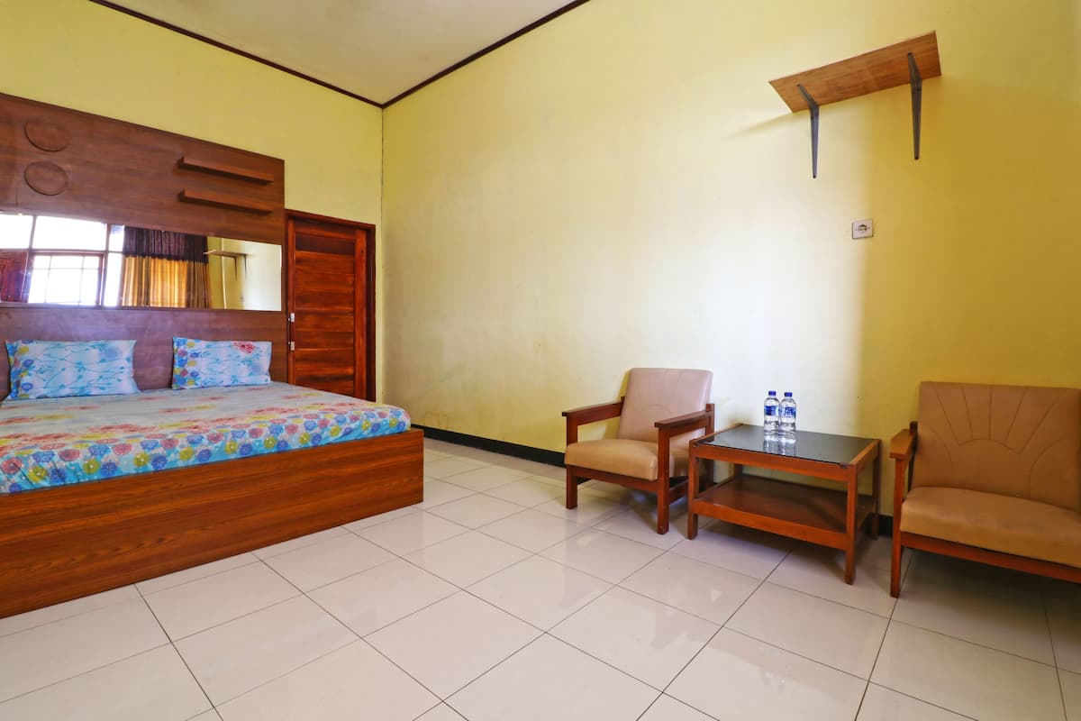 A room with a wooden bed, two chairs, a small table, and a mirror on the wall.