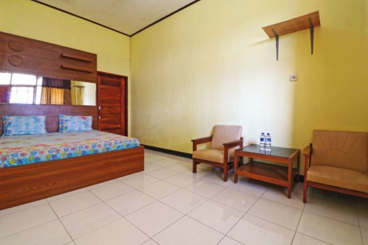 A bedroom with a bed, a chair, a small table, and a wooden shelf.