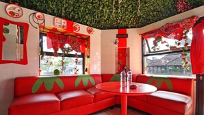 A red sofa and a round table in a room with a green leafy ceiling and a window with red curtains. - Hotel Agung Permata Artha (Garut)