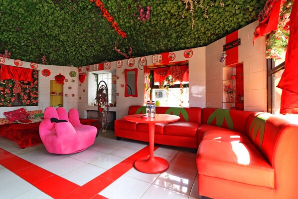 Una habitación vibrante con un techo cubierto de follaje verde, paredes rojas y blancas, y un sofá rojo.