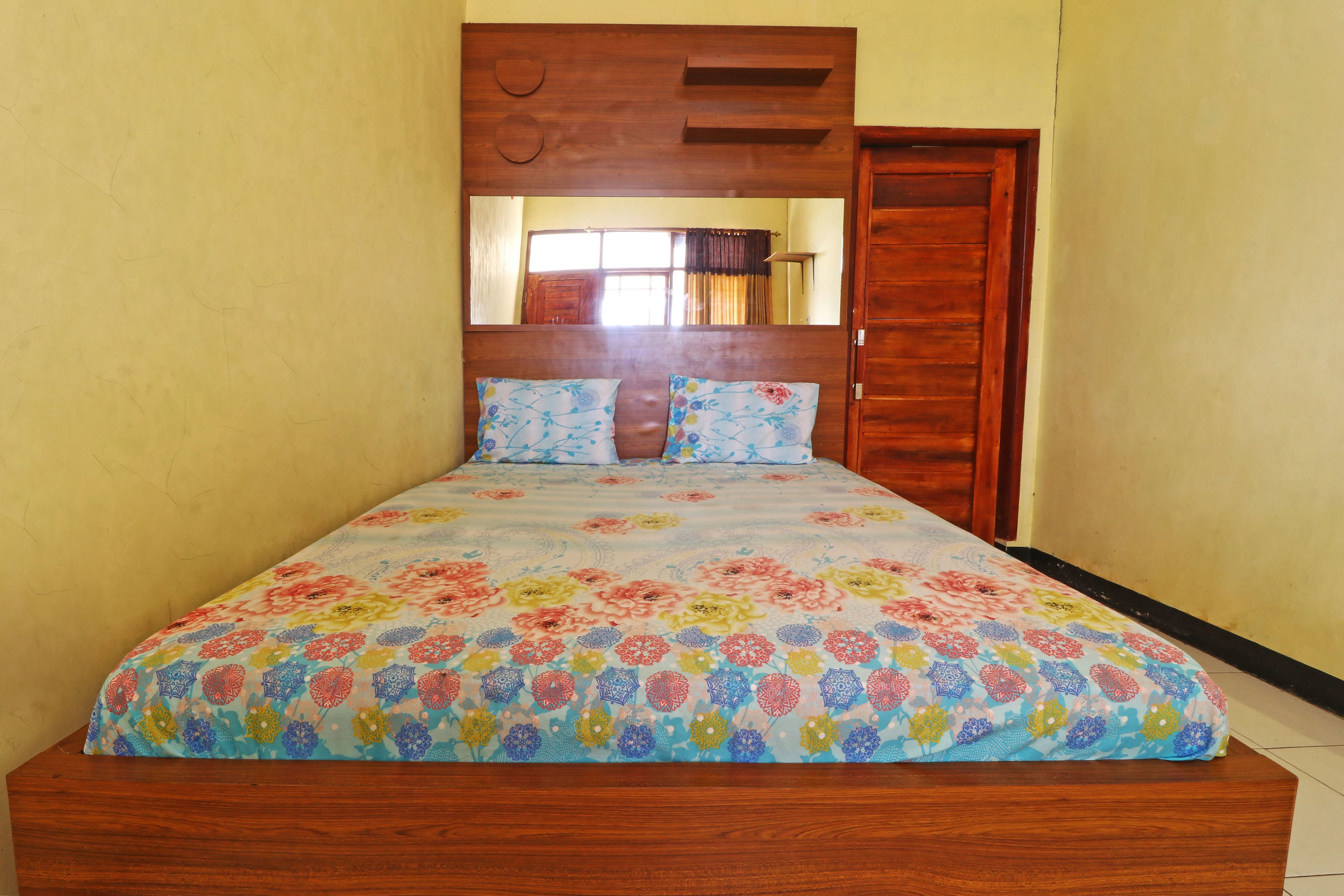 Un dormitorio con cabecera de madera, colcha estampada y puerta de madera.