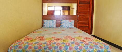 Un dormitorio con cabecera de madera, colcha estampada y puerta de madera.