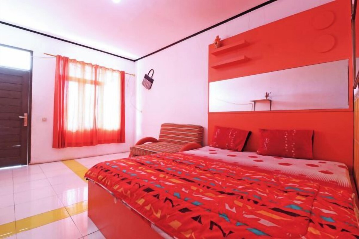 A bedroom with a large bed, a chair, a bedside table, and a window with curtains.