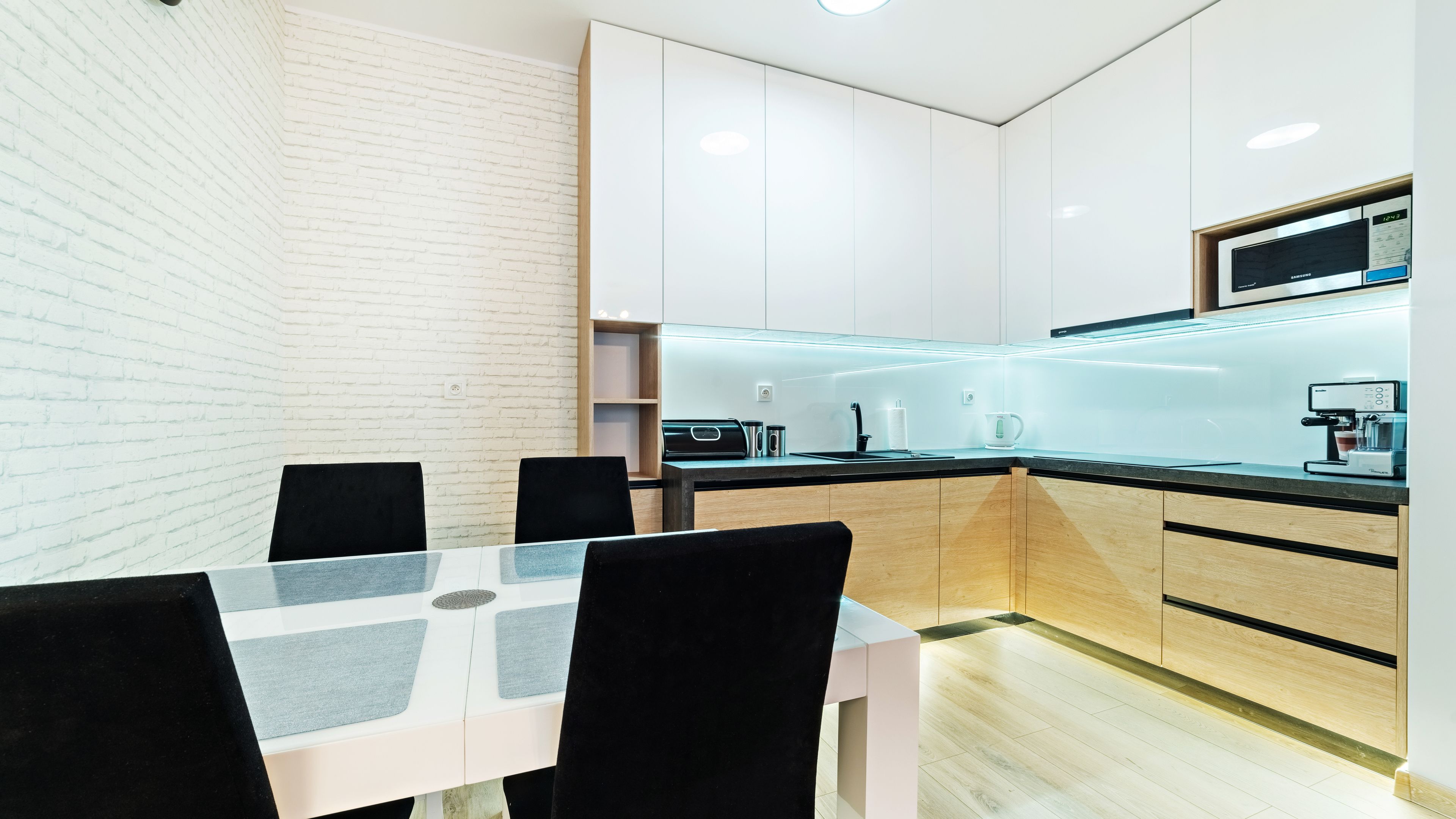 Una cocina moderna con armarios blancos, una encimera negra y una mesa de comedor con sillas.