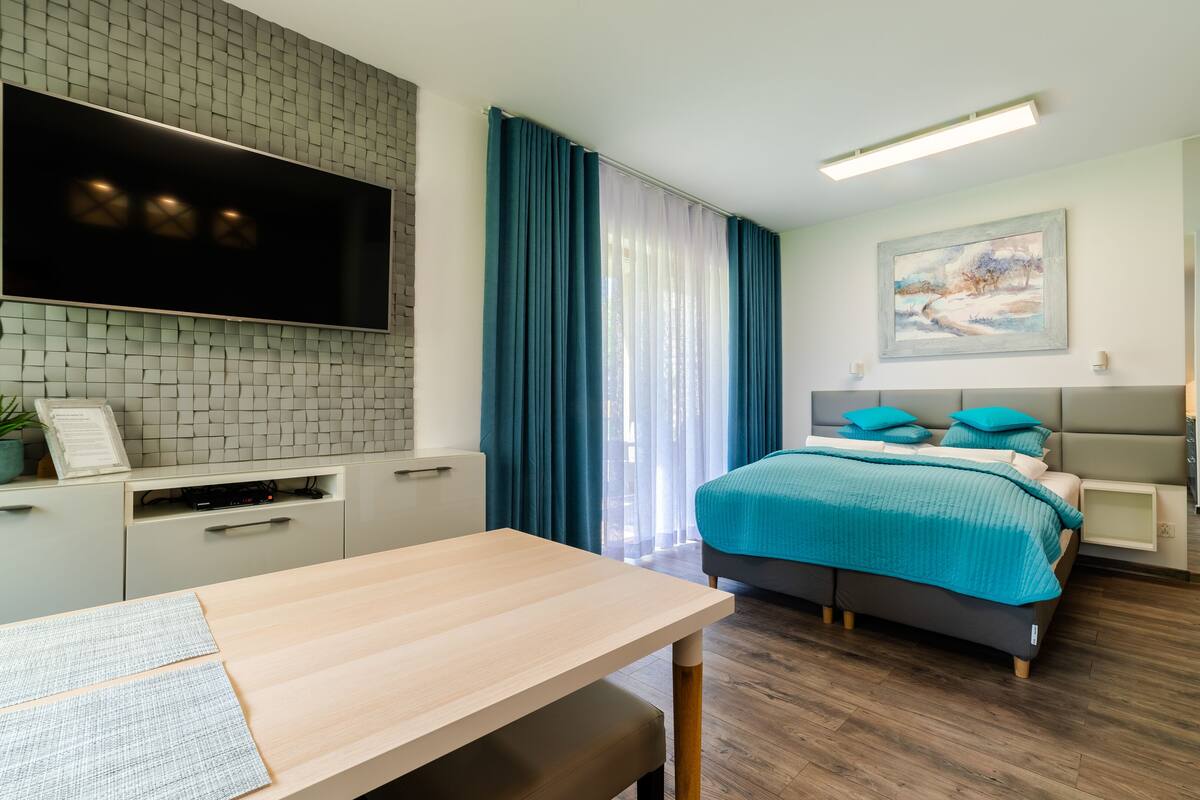 A modern bedroom with a bed, bedside tables, a desk, and a TV mounted on a wall.