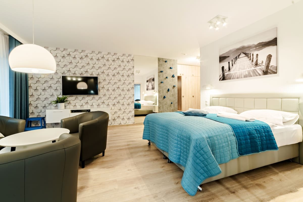 A modern hotel room with a bed, a desk, a chair, a TV, and a painting on the wall.
