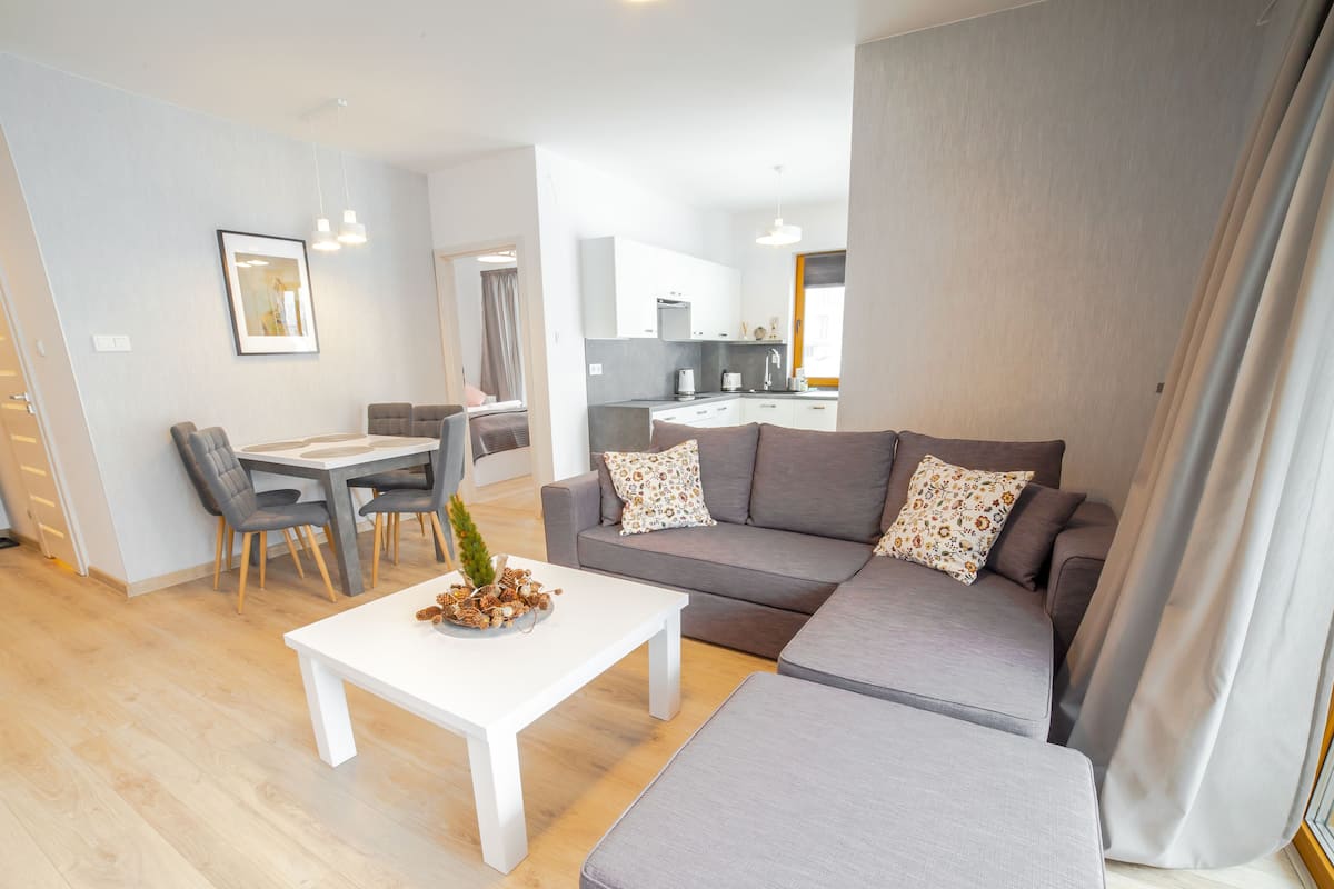 A modern living room with a grey sofa, a white coffee table, and a dining area with a table and chairs.