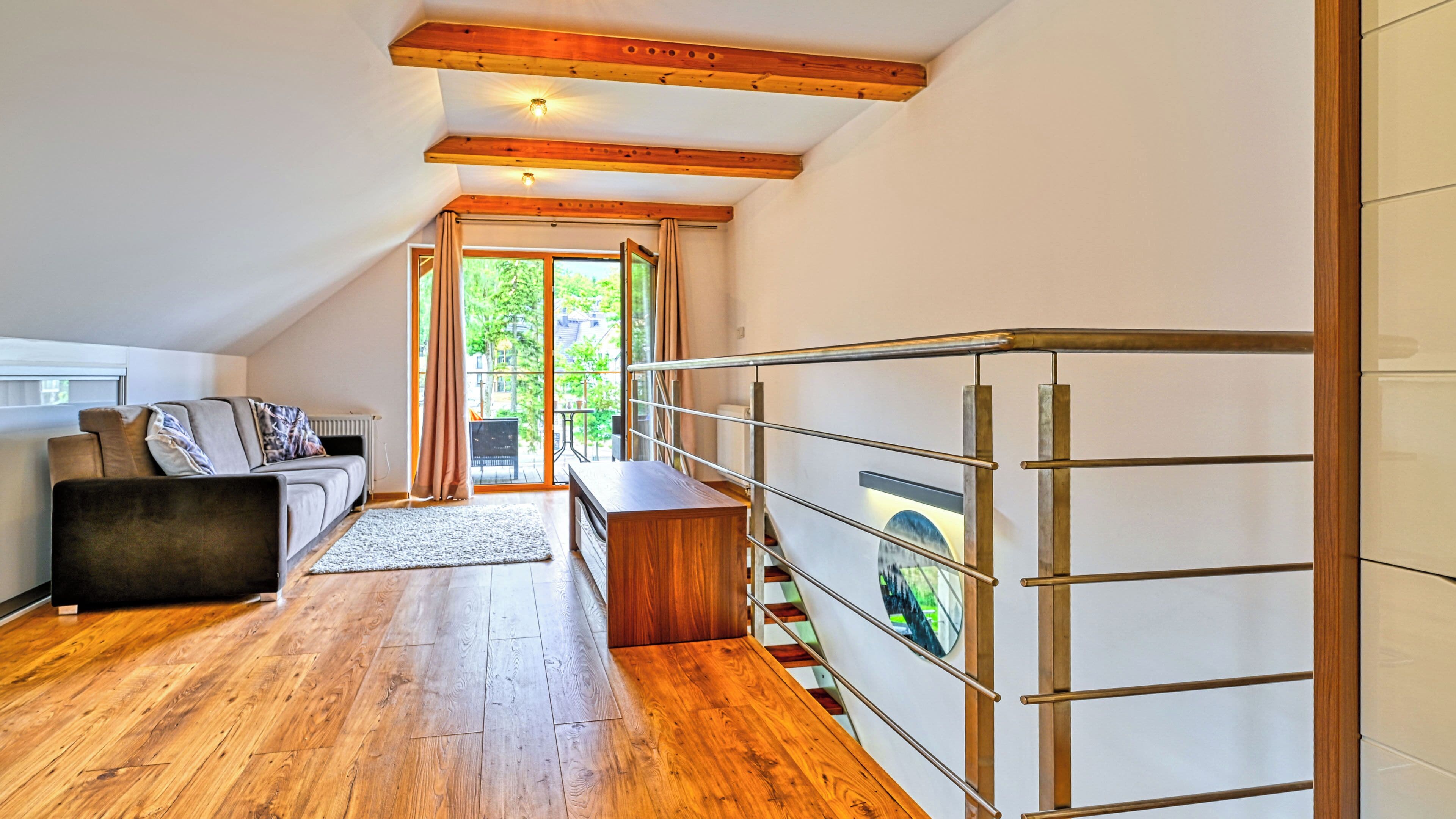 A modern interior with a wooden floor, a sofa, a dining table, and a staircase with a metal railing.