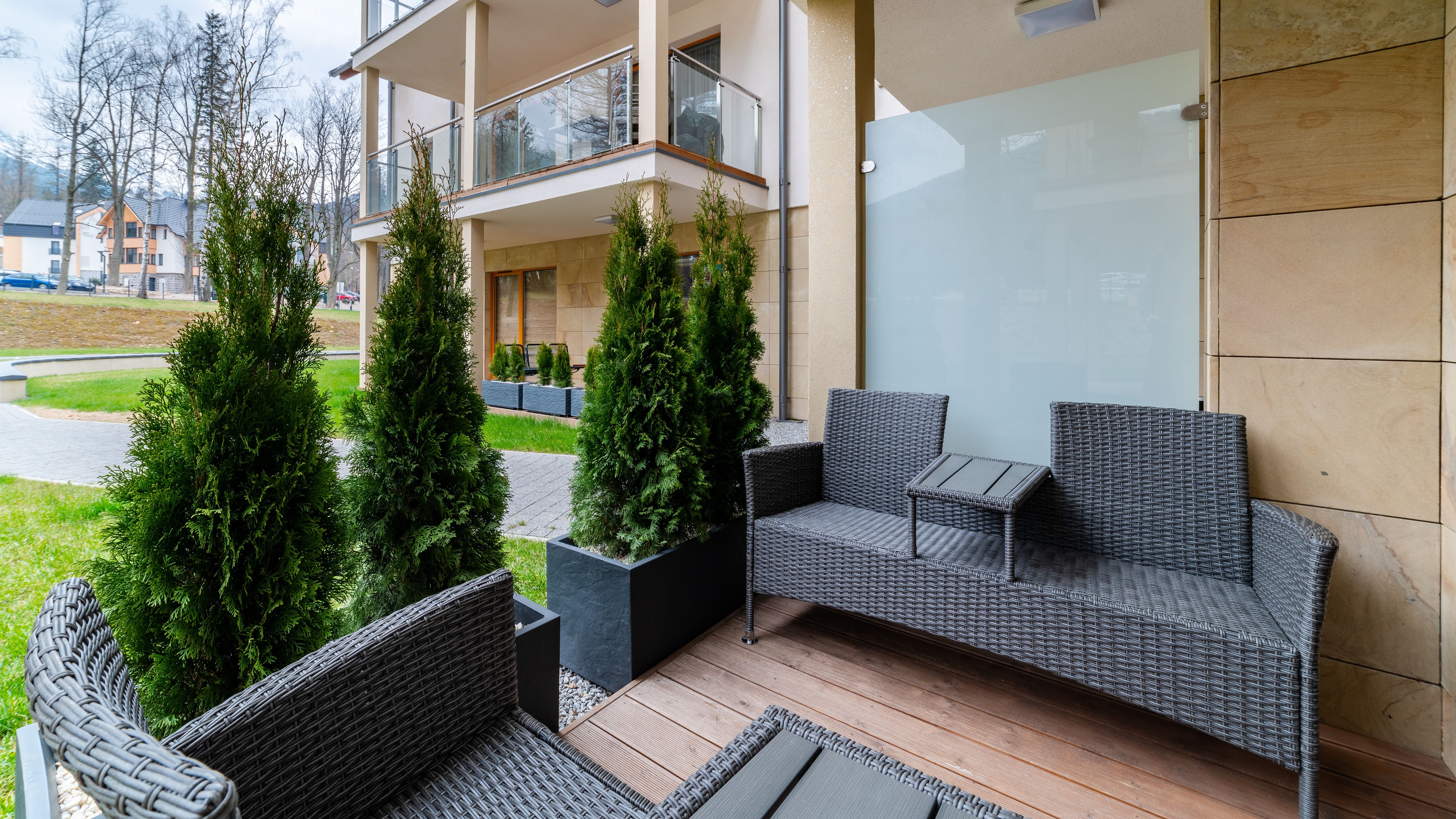 A modern outdoor seating area with wicker furniture and potted evergreen trees.
