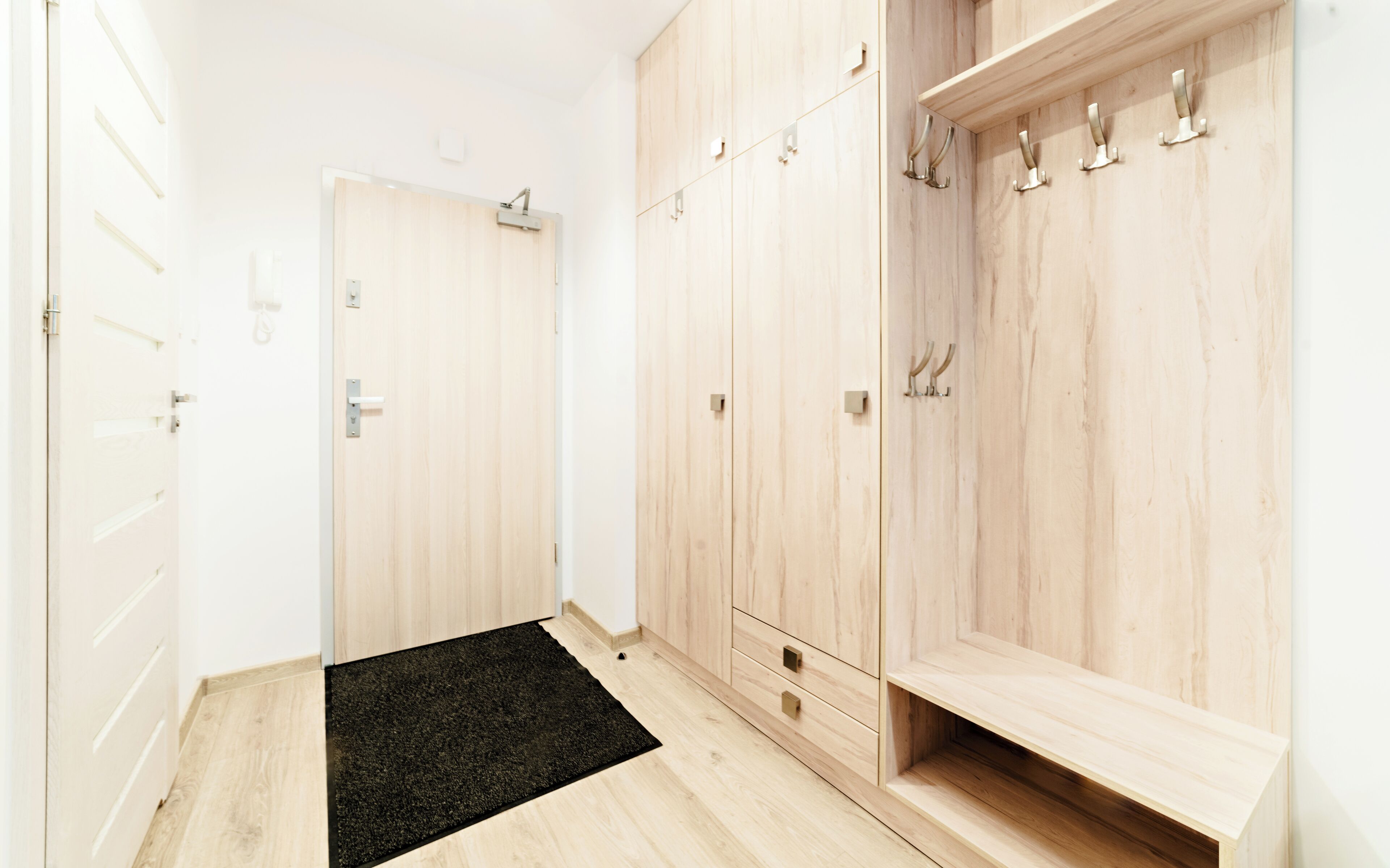 A hallway with wooden wardrobes, a black doormat, and a white door.