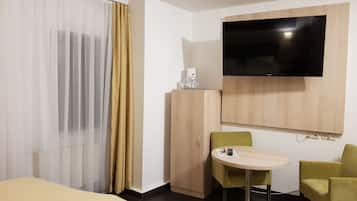 A hotel room with a bed, a desk with a chair, a television mounted on the wall, and a wardrobe.