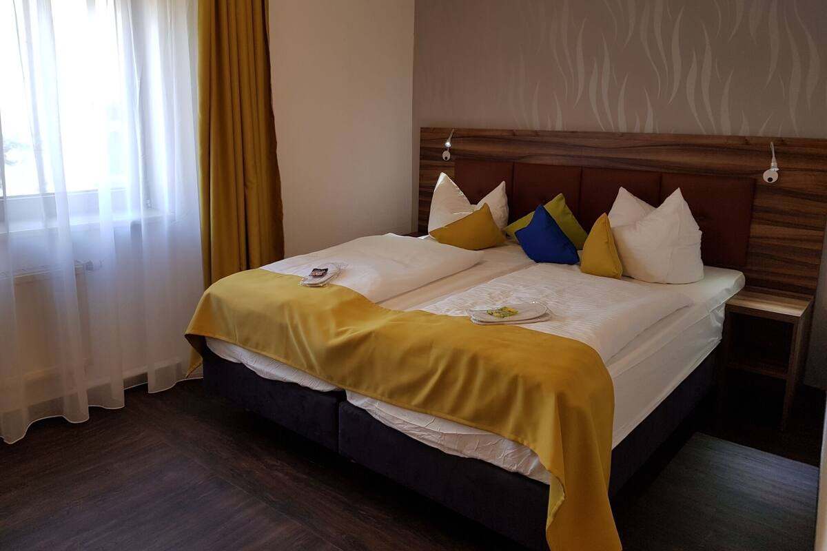 A double bed with a wooden headboard, white bedding, and yellow and blue pillows.