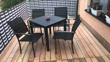 Une terrasse en bois avec une table noire et quatre chaises, une clôture à rayures et des plantes en pot sur un rebord de fenêtre.