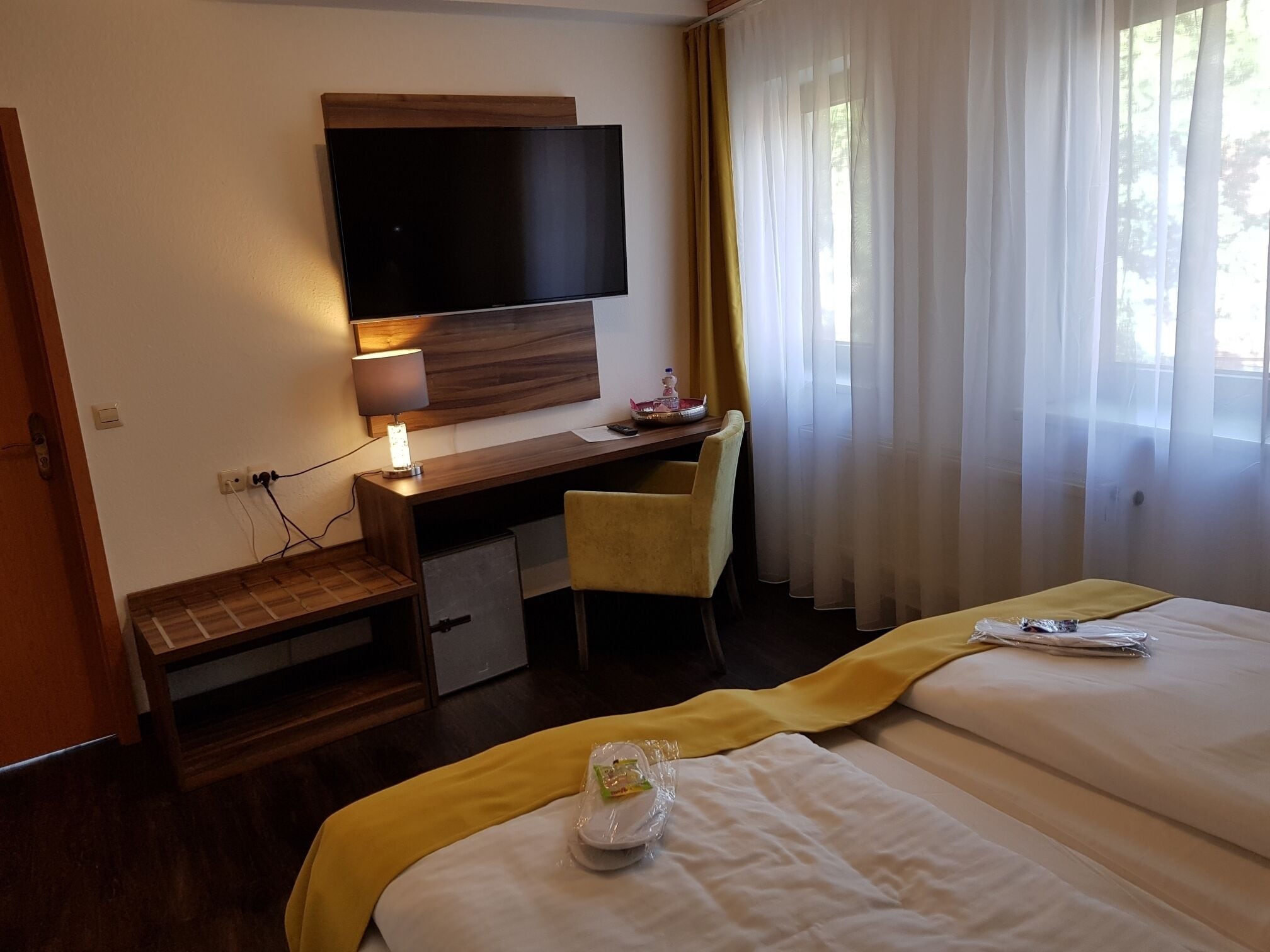 Una habitación de hotel con cama, escritorio con silla, televisor y ventana con cortinas.