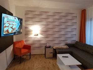 Una sala de estar moderna con un televisor de pantalla plana, un sofá, una mesa de centro y una mesita auxiliar con una botella.