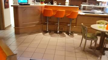 A bar area with orange bar stools, a counter with a computer, and a dining area with a round table and chairs.