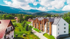 Una hilera de edificios modernos de varios pisos con balcones, rodeada de abundante vegetación y montañas al fondo.