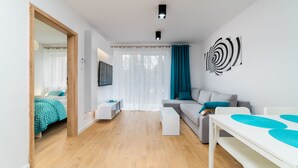 Un salón moderno con un sofá gris, una mesa de centro blanca y un televisor montado en la pared.