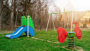 Un parque infantil con un tobogán azul, una estructura de escalada verde y un juguete de resorte rojo.