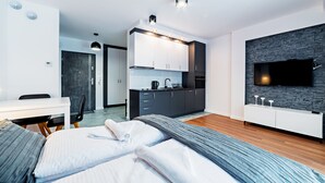 Una habitación de hotel moderna con cama, escritorio, kitchenette y televisor montado en una pared con textura de piedra.