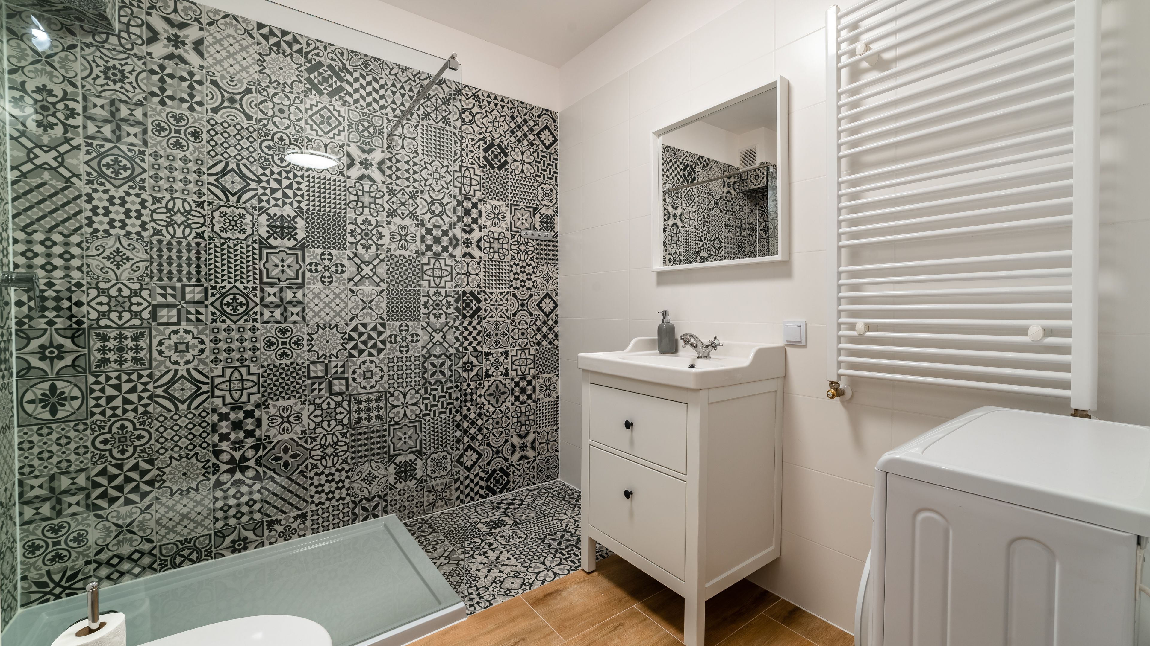 Un bagno con piastrelle decorate, un lavandino, uno specchio e un termosifone.