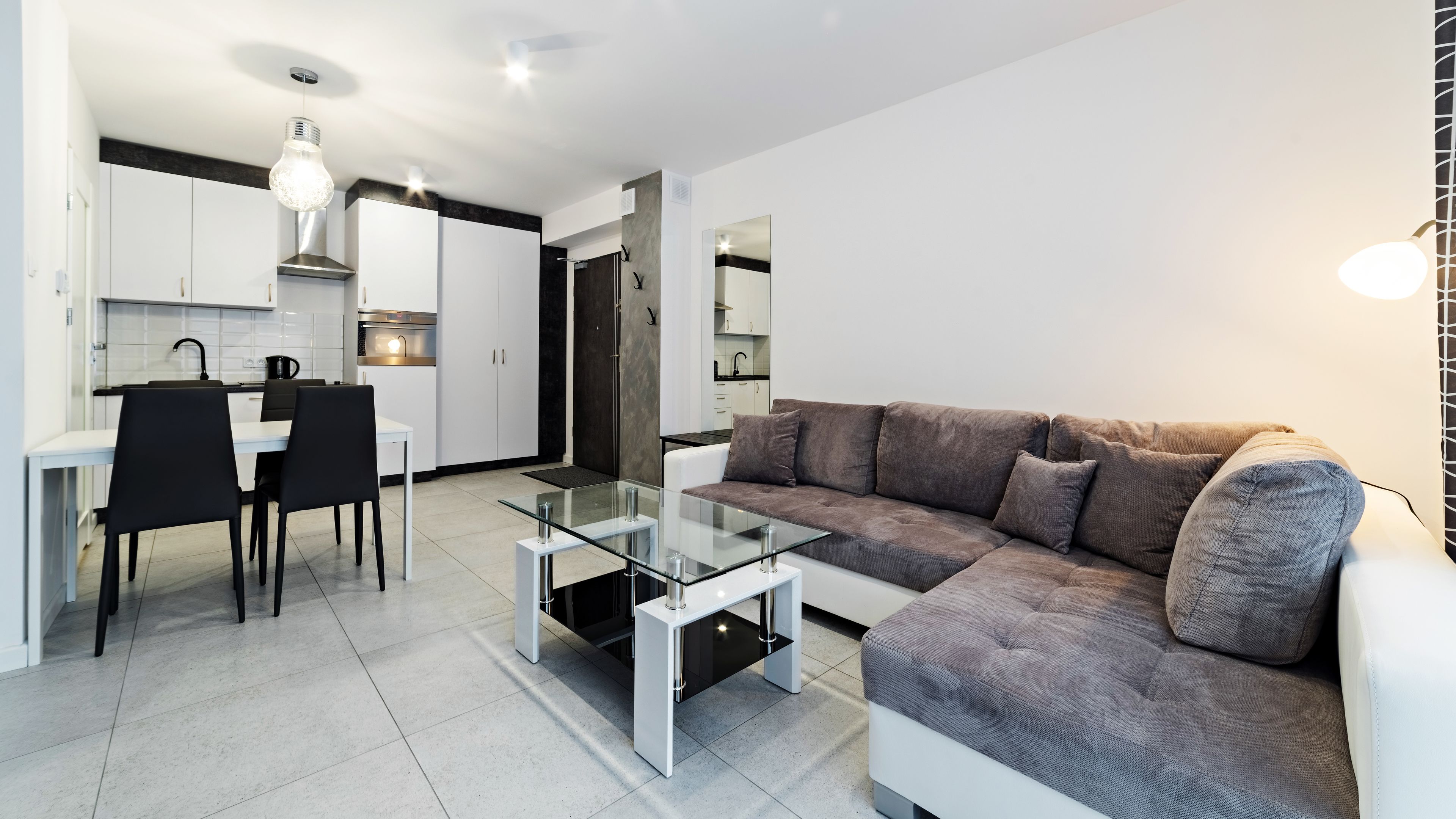 Een moderne woonkamer met een glazen salontafel, een grijze bank en een eethoek met zwarte stoelen.