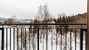 Un paisaje nevado con árboles desnudos y una vista distante de casas y montañas.