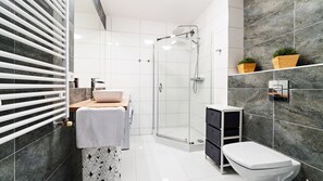 Un baño moderno con cabina de ducha de vidrio, un lavabo blanco y un inodoro.
