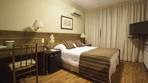 A hotel room with a bed, a desk with a chair, a TV, and an air conditioning unit. - Hotel Salto Grande (Concordia)