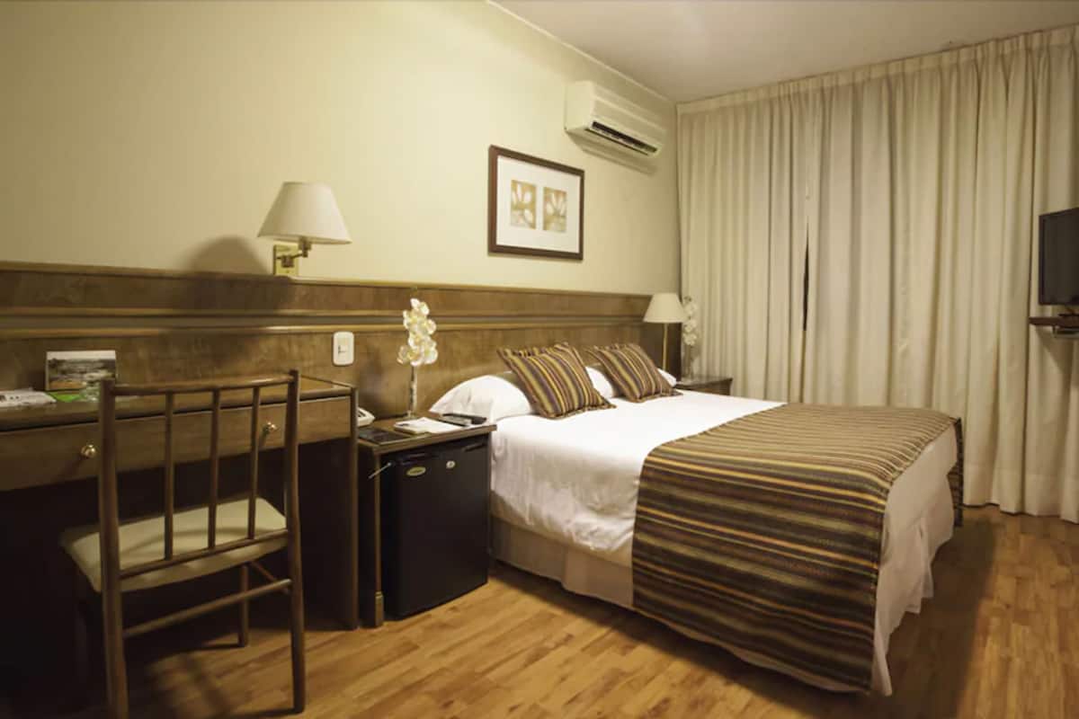 Ett hotellrum med en säng, ett skrivbord med en stol, en TV och en luftkonditioneringsanläggning.
