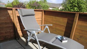 A sun lounger with a cushion, positioned on a tiled patio with a wooden fence in the background. - Böltser Hus (Neukirchen)
