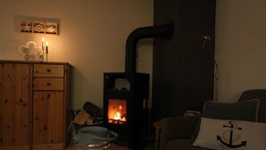 A cozy living room with a wood-burning stove, a wooden cabinet, and a couch with striped pillows. - Böltser Hus (Neukirchen)