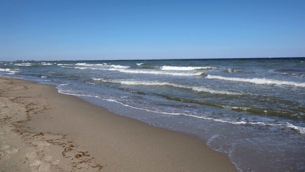 A beach with waves, a clear sky, and a distant sailboat. - Böltser Hus (Neukirchen)