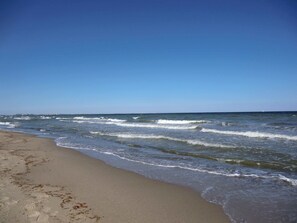 A beach with waves, a clear sky, and a distant sailboat. - Böltser Hus (Neukirchen)