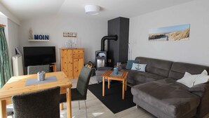 A living room with a sofa, a TV, a wooden table, and a fireplace. - Böltser Hus (Neukirchen)