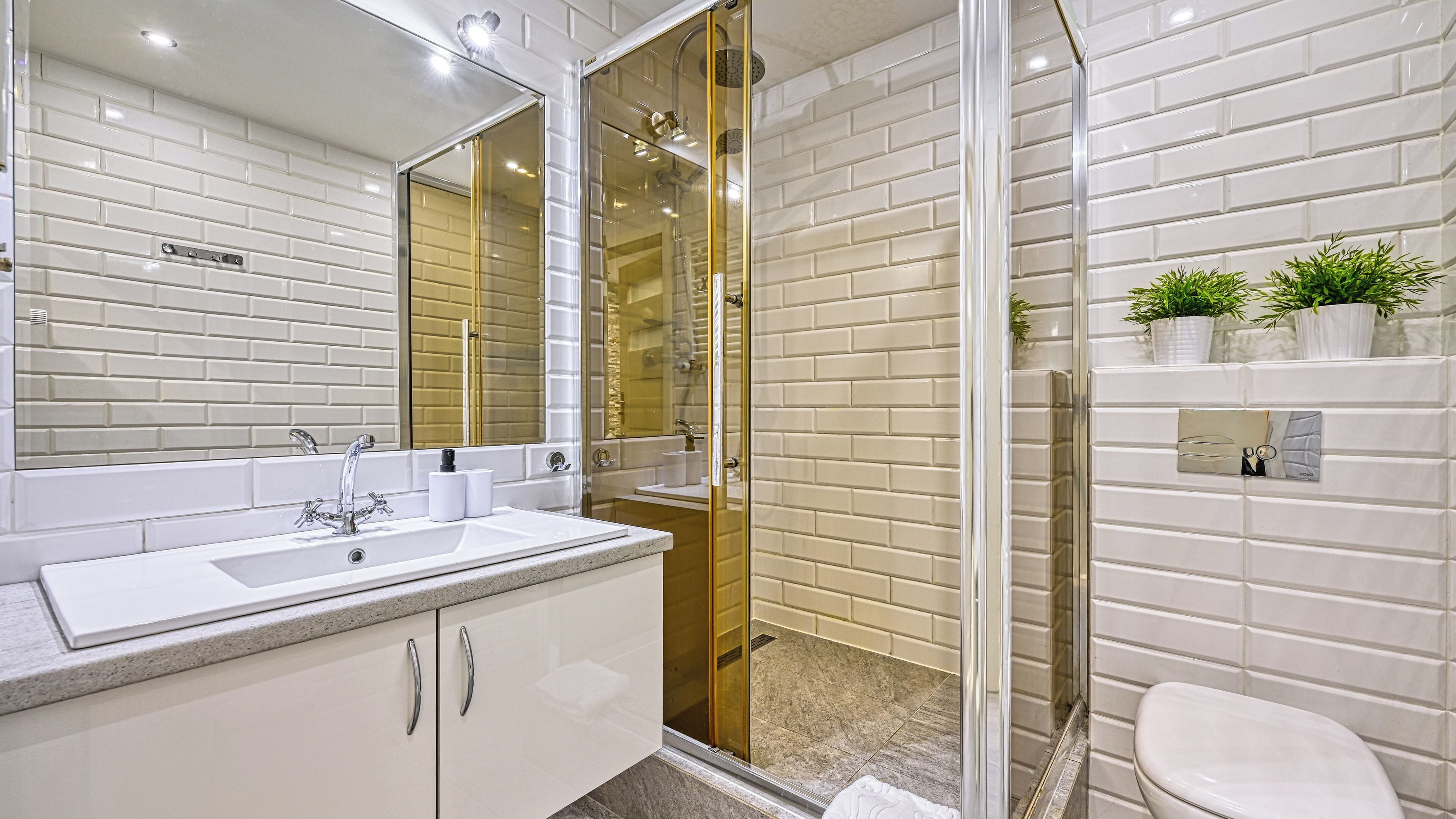 Une salle de bain moderne avec un mur recouvert de carreaux de métro blancs, un grand miroir, une douche à parois de verre et des toilettes.