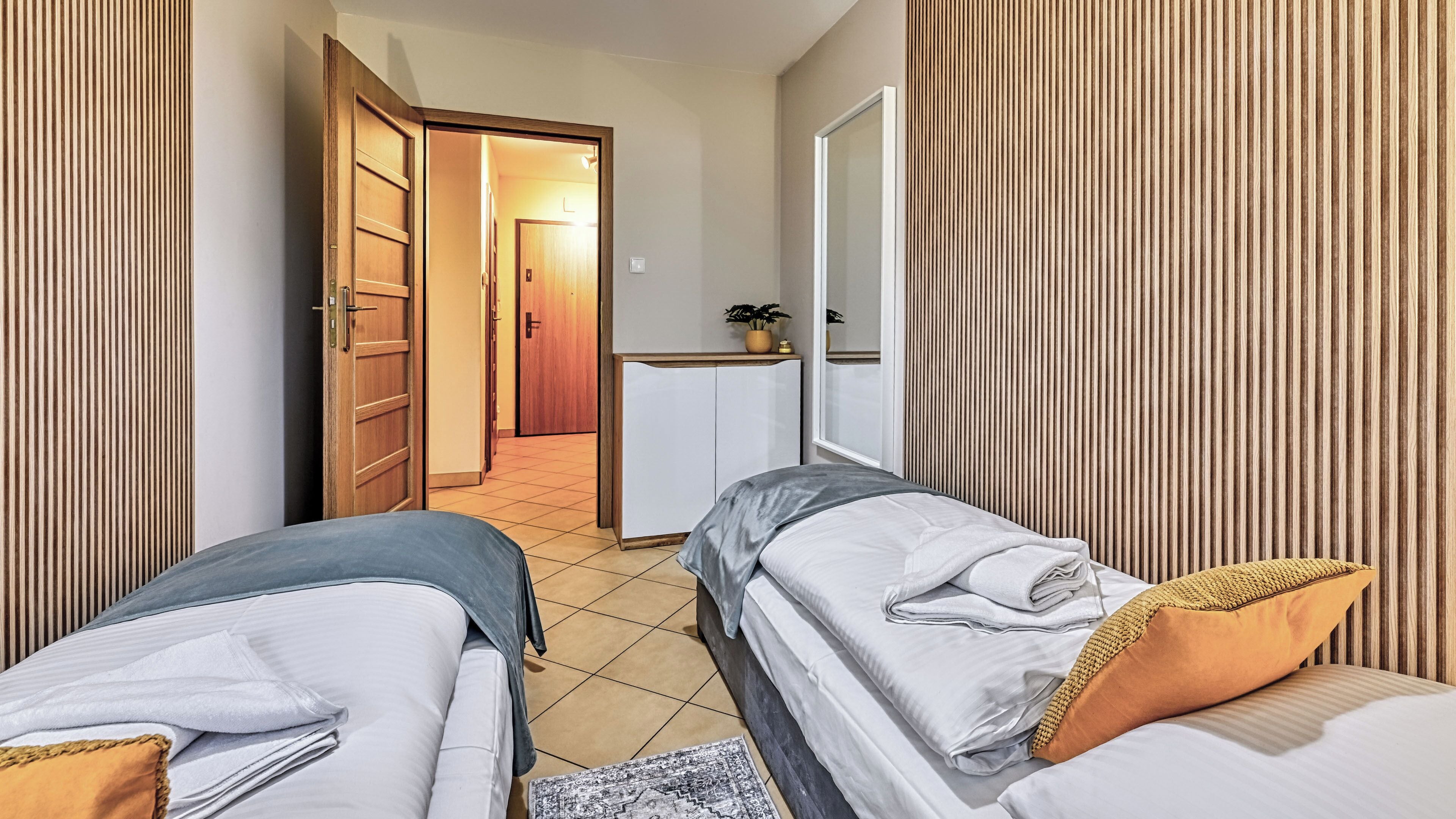 A hotel room with two beds, a desk, a wardrobe, and a door leading to a hallway.