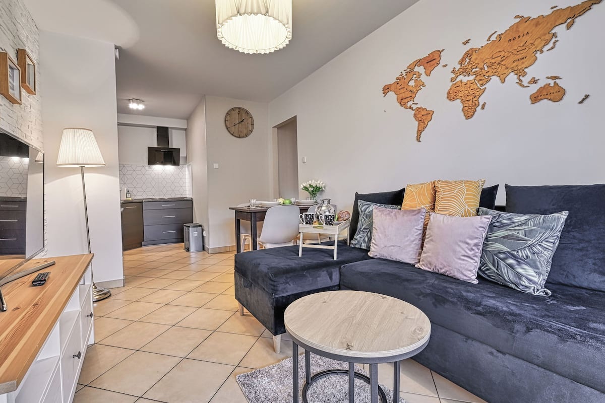 Una sala de estar moderna con un sofá oscuro, una mesa redonda y un mapa del mundo en la pared.