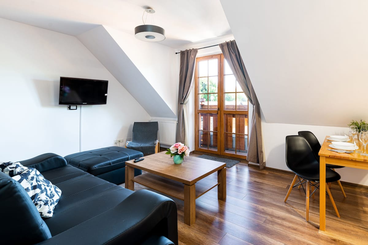 Una sala moderna con un sofá, una mesa de comedor para dos personas y un televisor montado en la pared.
