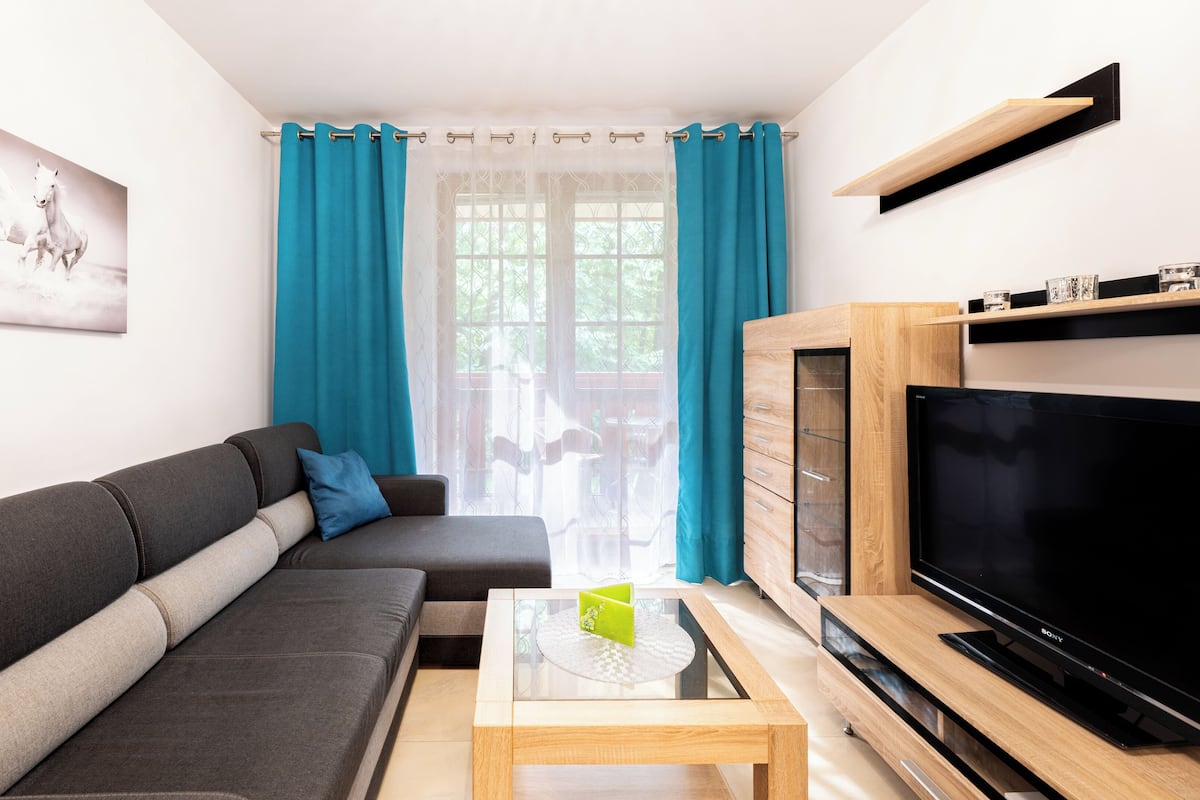 Un salón moderno con un sofá gris, una mesa de centro, un televisor de pantalla plana y un mueble de madera.