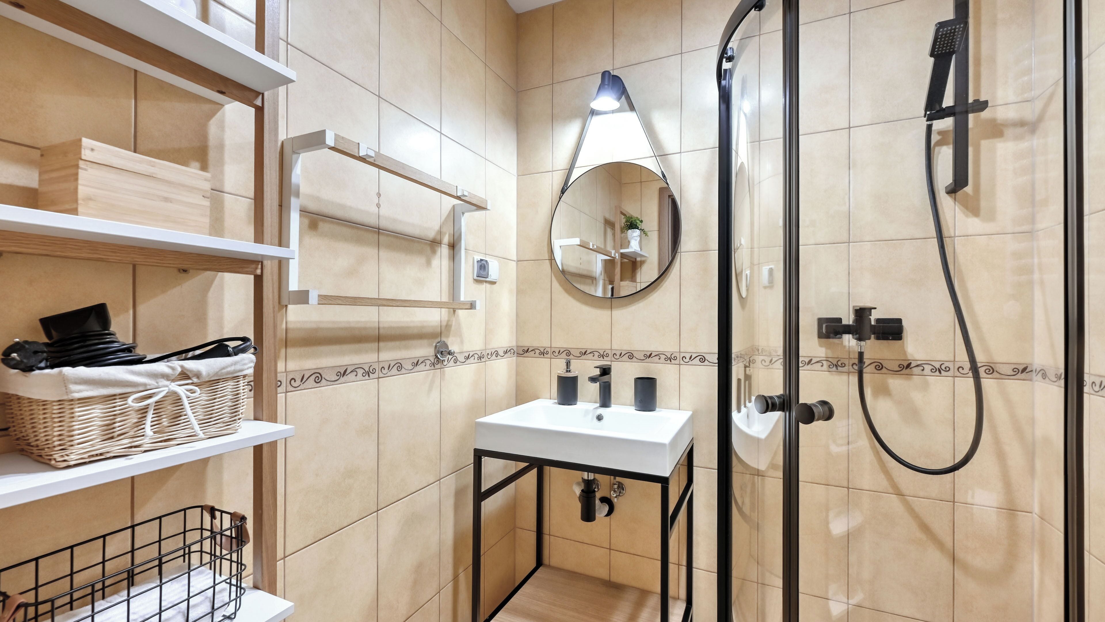 A bathroom with a white sink, a mirror, a shower, and shelves with toiletries.
