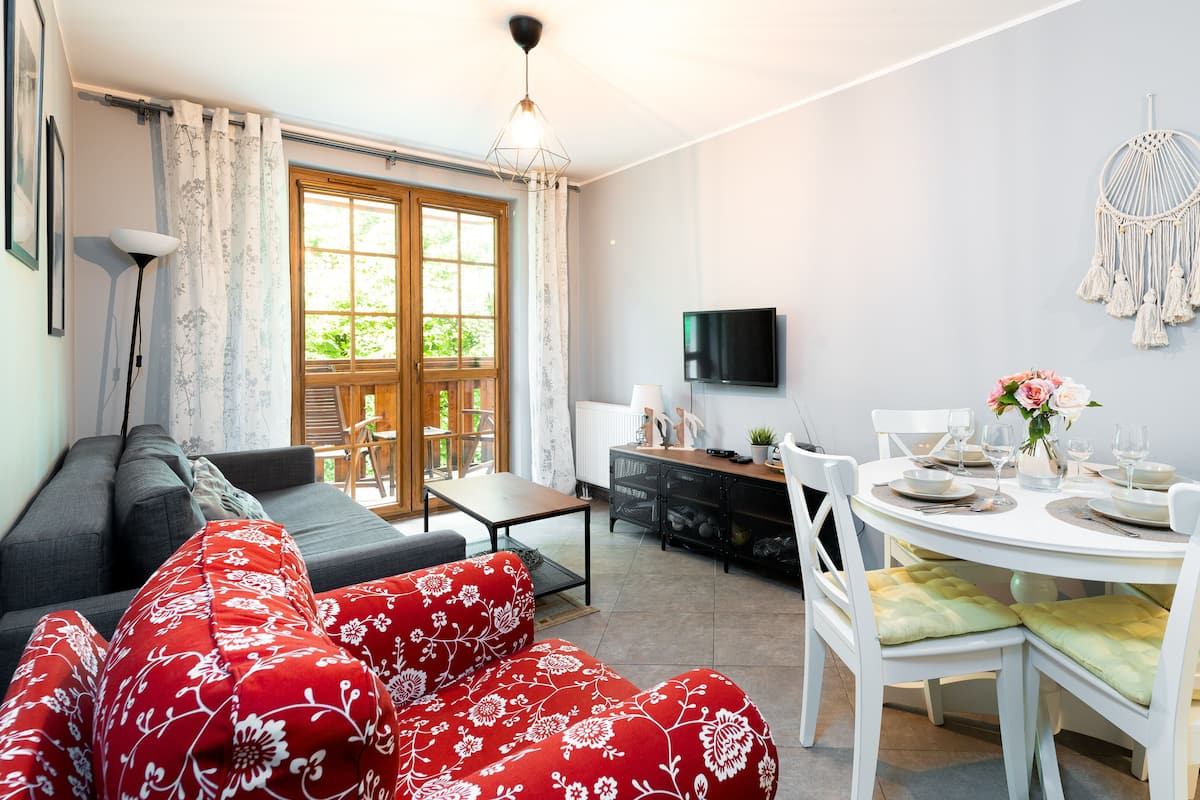 Una sala de estar con un sofá, una mesa de comedor para cuatro personas y un televisor montado en la pared.
