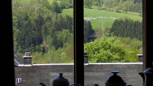 A view through a window of a rural landscape with rolling hills, a small village, and a clear sky. - Hotel Goldene Sonne (Annaberg-Buchholz)