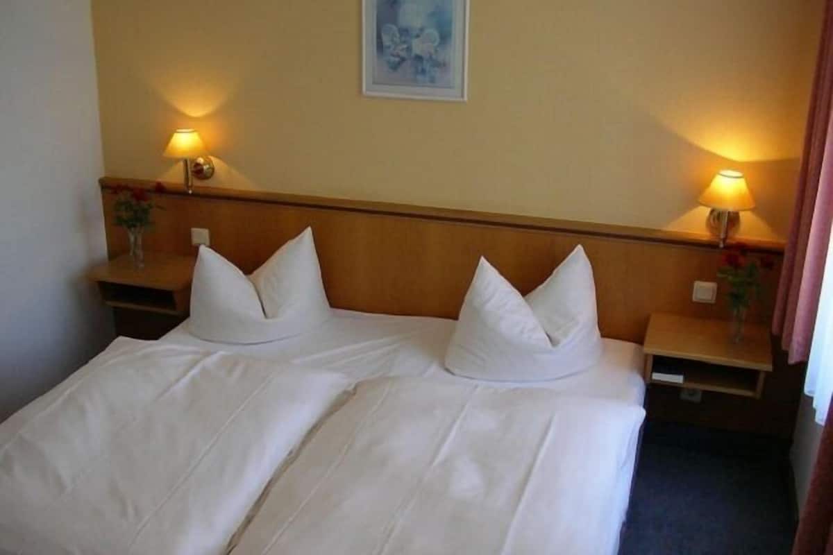 A double bed with white linens, two bedside tables with lamps, and a framed picture on the wall.