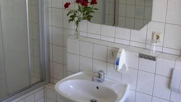 Ein Badezimmer mit einem weißen Waschbecken, einem Spiegel und einer Vase mit roten Blumen.