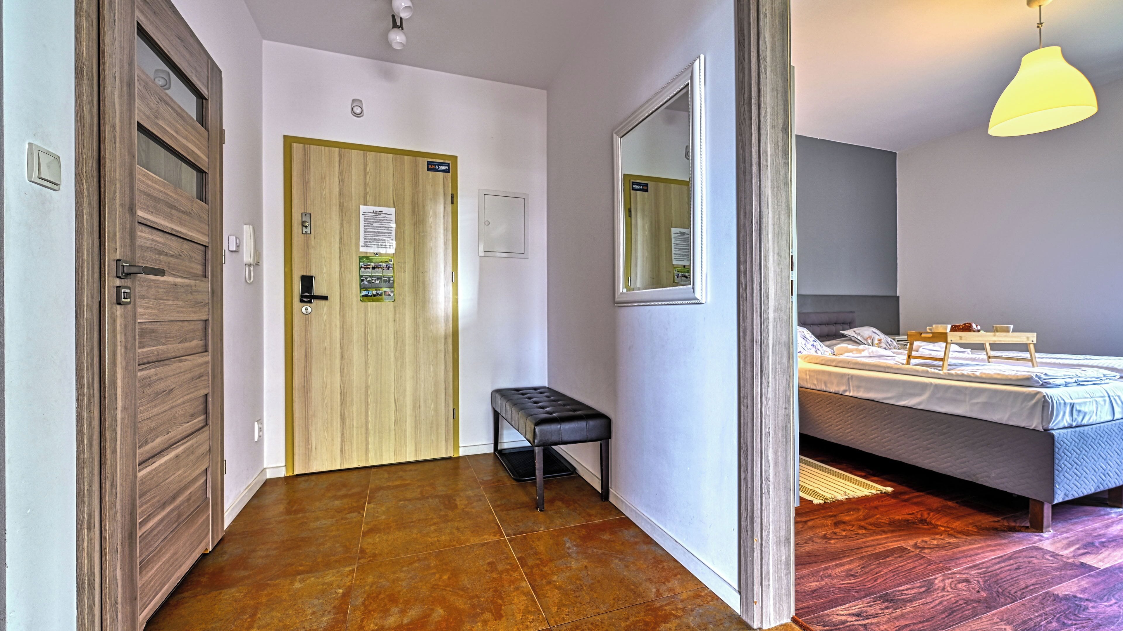 Habitación de hotel con una cama, un banco, una puerta de madera y un espejo en la pared.
