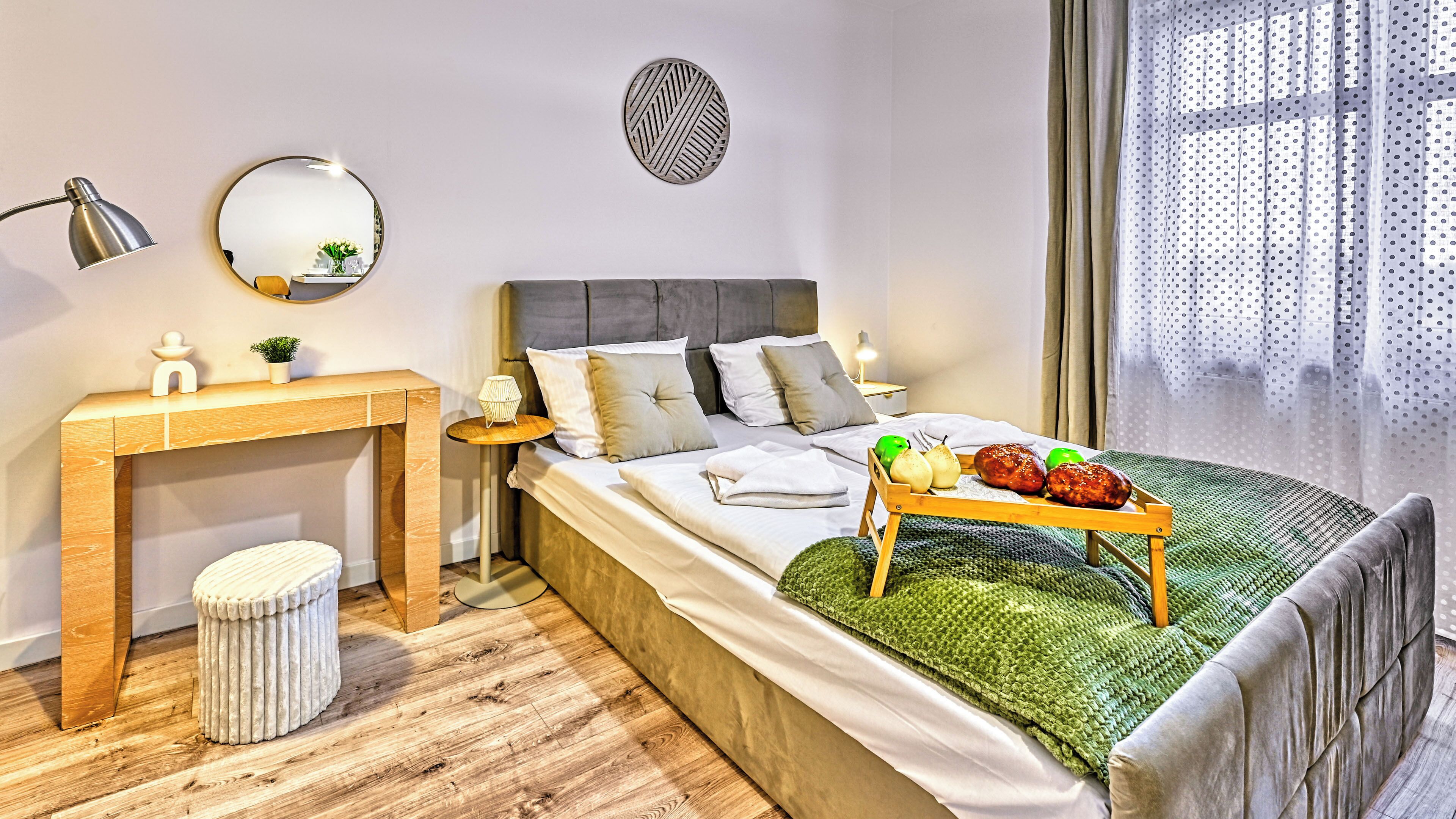 Une chambre à coucher avec un lit, une table de chevet, une lampe, un miroir et un plateau contenant des fruits et des légumes.