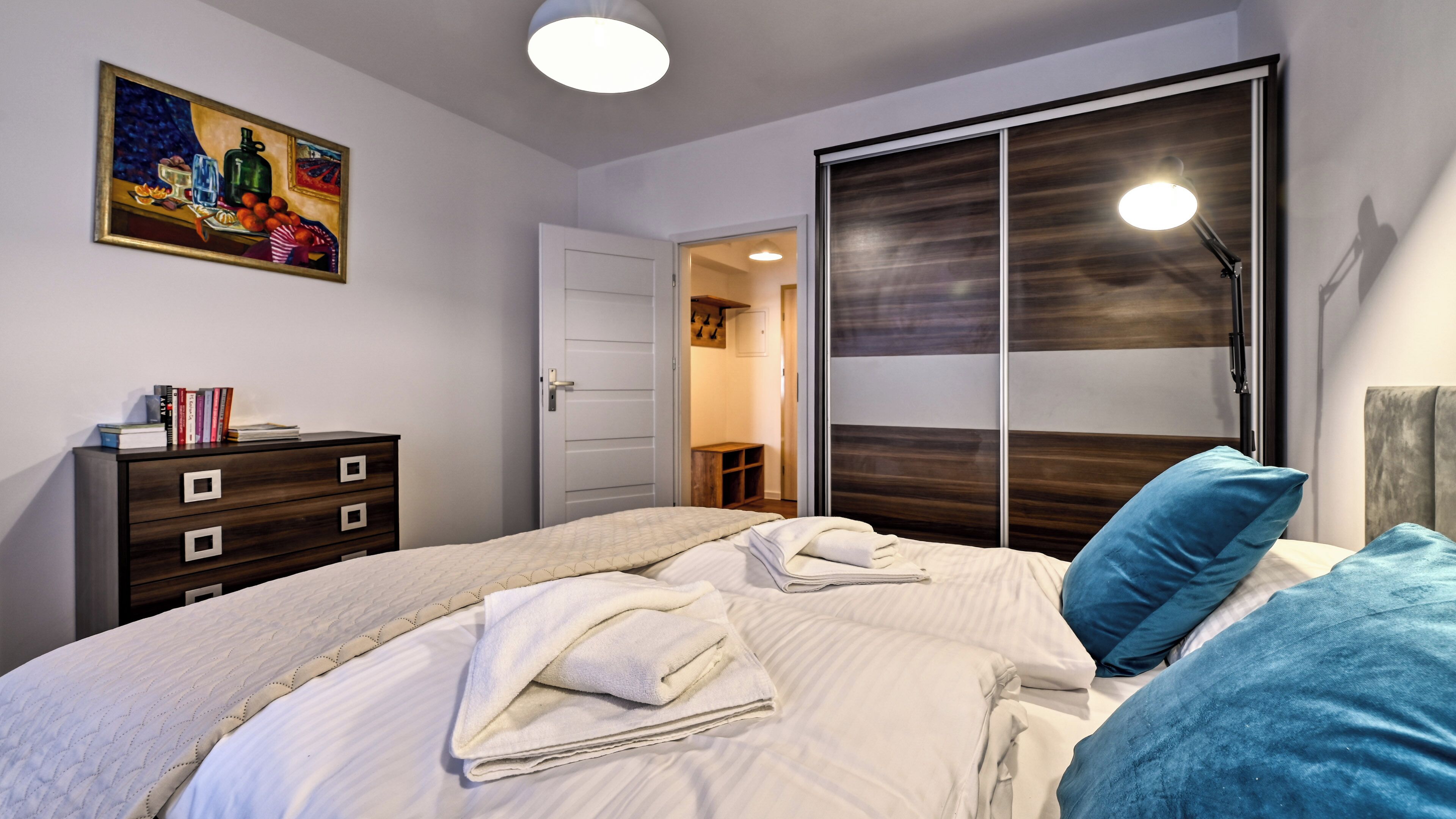 A bedroom with a bed, a dresser, a painting, and a wardrobe.